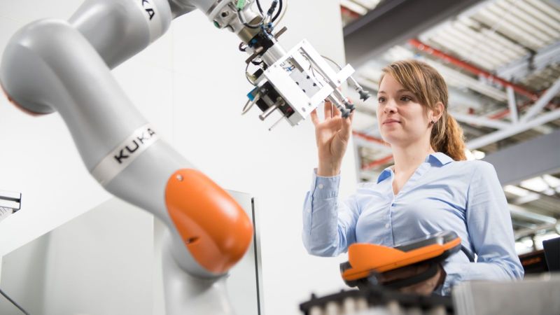 Eine junge Frau programmiert einen Roboter, der in der Produktion kleinere Losgrößen ermöglicht.