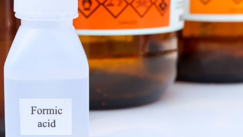 Ameisensäure in einem kleinen Plastikbehälter vor braunen Glasflaschen