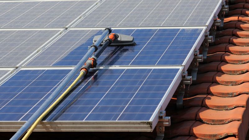 Photovoltaikanlage auf dem Dach: ein Solarmodul wird mit einem speziellen Gerät von Staub befreit.
