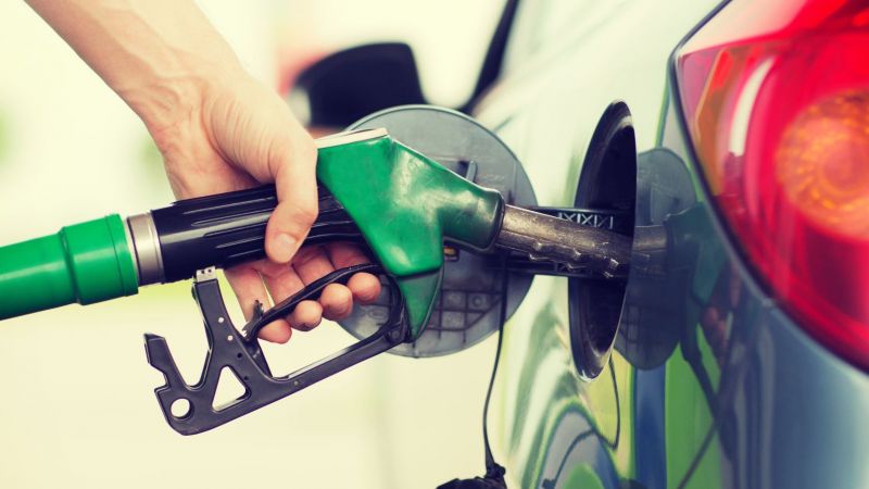 Nahaufnahme einer Hand, die eine Zapfpistole in die Tankklappe eines Autos steckt