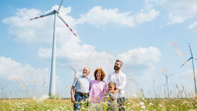 Großeltern, Vater und Tochter stehen lachend auf einem Feld vor Windrädern