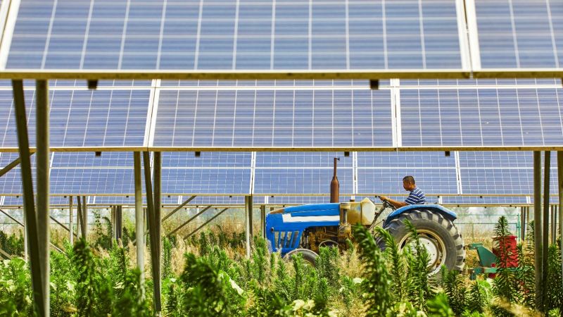 Landwirt fährt mit Traktor auf Feld mit Solarmodulen
