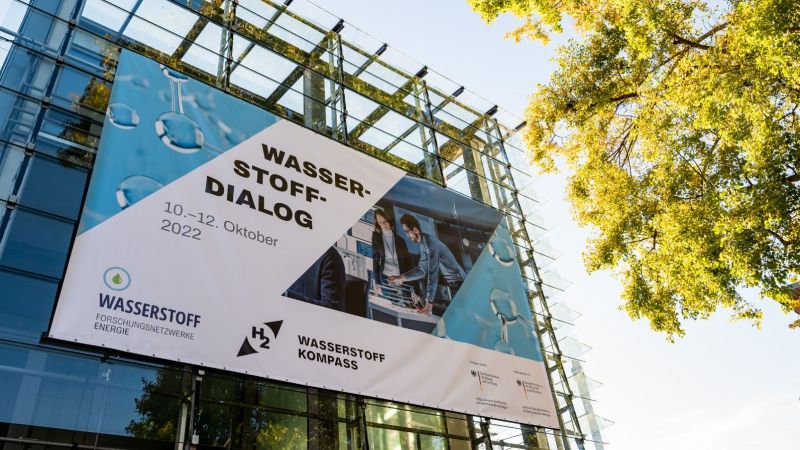 Ein Plakat zur Ankündigung des Wasserstoff-Dialogs hängt an einer Gebäudefassade.