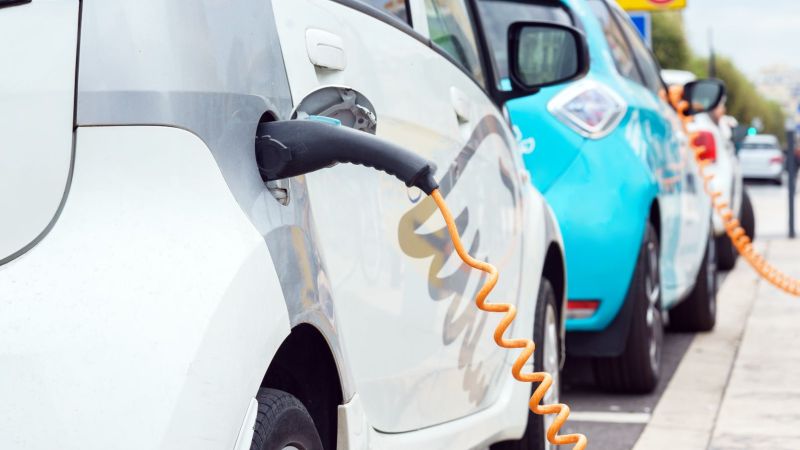 Nahaufnahme eines ladenden Elektrofahrzeugs: Eine elektrische Zapfpistole steckt in einem offenen Tankdeckel.