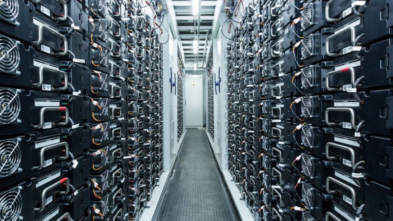 Raum mit einem schmalen Flur in der Mitte; rechts und link stehen Batteriespeicher, die aussehen wie Schränke.
