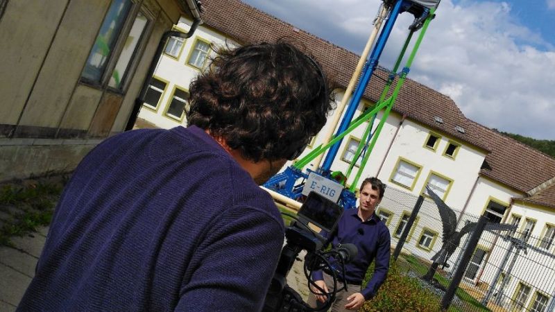 Ein Kameramann filmt einen der Protagonisten des Films „Energy for Tomorrow – Innovative Geothermal Technology“ vor einer Versuchsanlage.