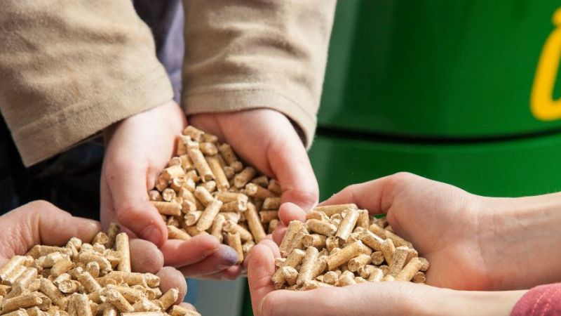 Es sind Holzpellets in Händen abgebildet. Im Hintergrund steht ein Pelletkessel.