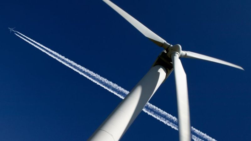 Flugzeug fliegt über einer Windenergieanlage.