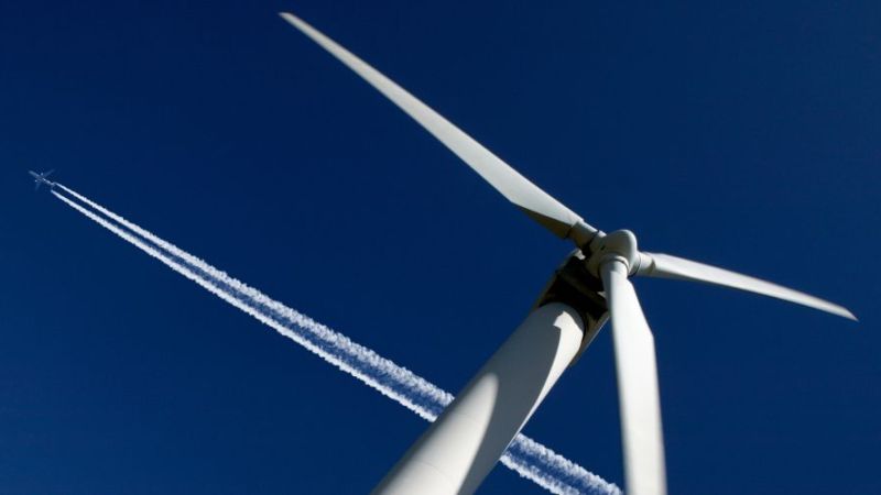 Aircraft flying over a wind turbine.