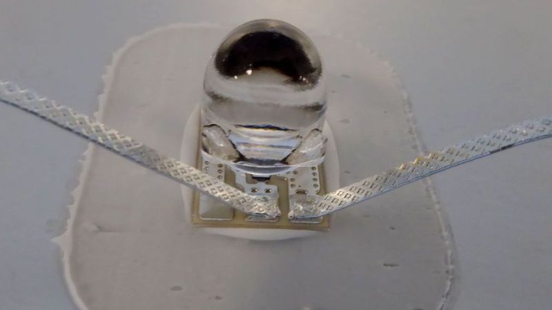 Ein Solarzellenassembly in einer Detailaufnahme. Zu sehen ist die optische Linse, die über der kleinen Solarzelle angebracht ist, zusammen mit den Drähten für die Verschaltung.