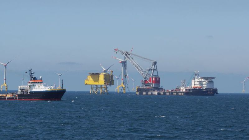Auf dem Foto sind mehrere Schiffe zu sehen, die gerade einen Offshore-Windpark aufbauen.