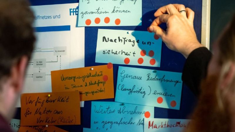 Zwei Personen hängen Notizen an eine Pinnwand.