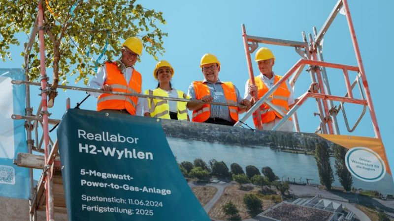 Vier Personen mit Bauhelm stehen auf einer Gerüst und feiern das Richtfest.