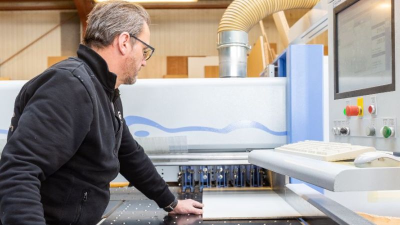 Arbeiter schneidet Brett an Anlage zurecht.