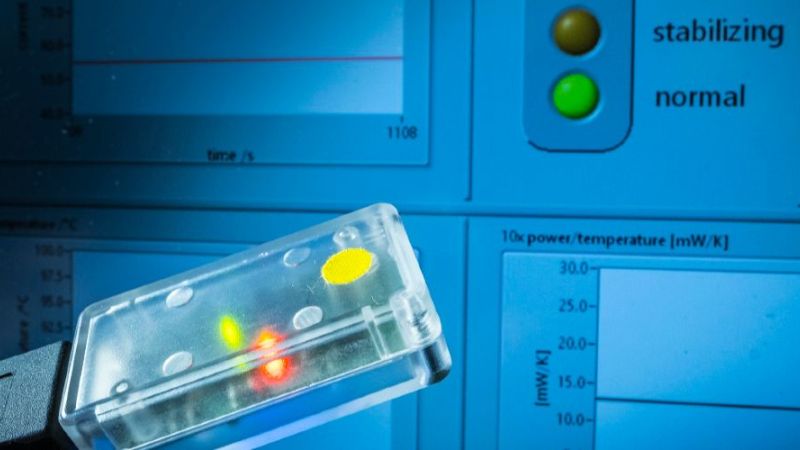 Sensorbaustein zur Wasserstoffdetektion vor einer digitalen Anzeige mit Ampelsystem für Sicherheitsstatus.