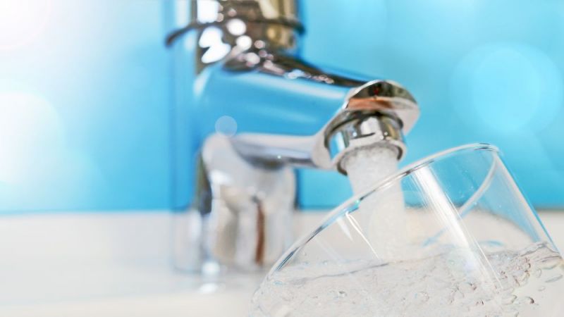 Wasser fließt aus Wasserhahn in Glas.