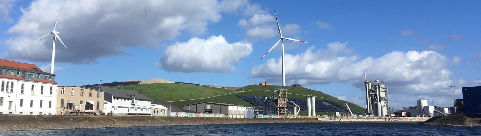 Blick vom Rheinhafen Karlsruhe auf den Energieberg mit zwei Windkraftanlagen und der Freiflächen-Photovoltaikanlage.
