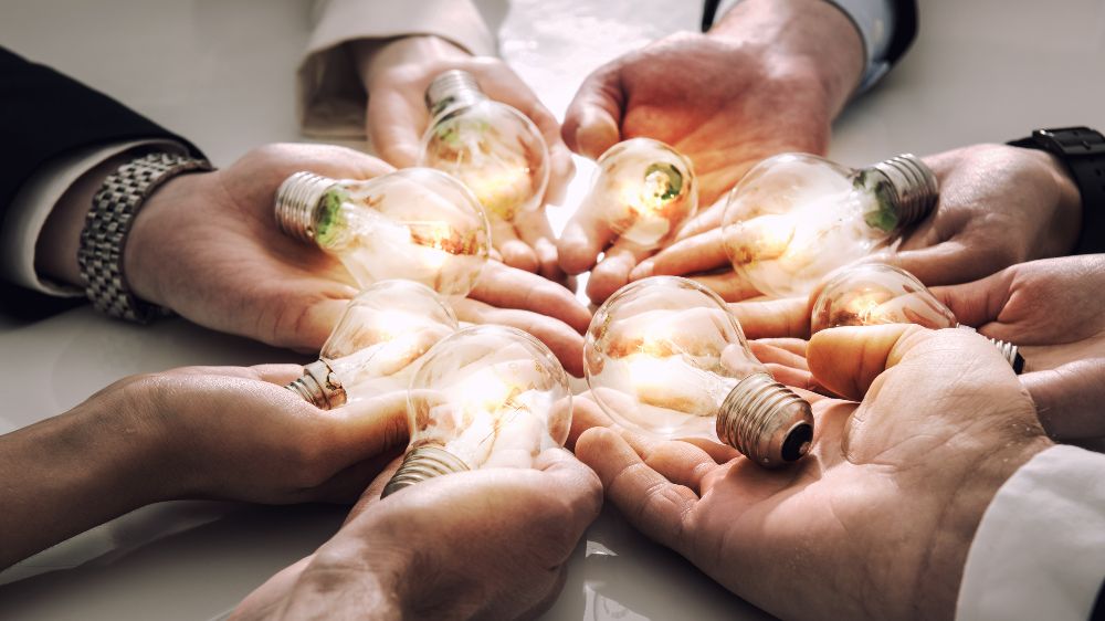 Symbolbild Teamwork: Mehrere Hände halten eine Glühbirne und formen einen Kreis