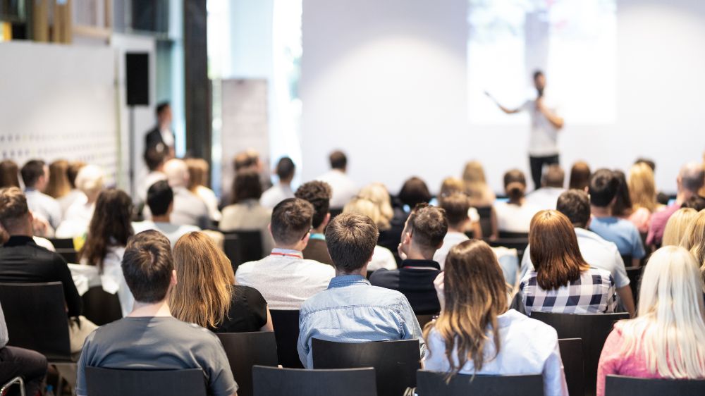 A conference room is blurred. People are sitting on chairs.
