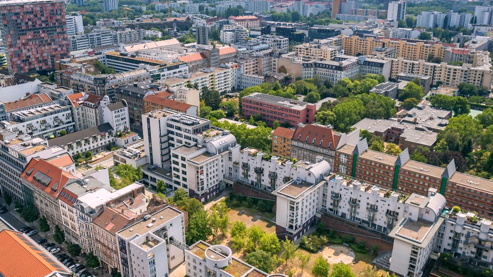 Luftaufnahme eines dicht bebauten Stadtviertels mit Wohn- und Bürogebäuden sowie begrünten Innenhöfen.