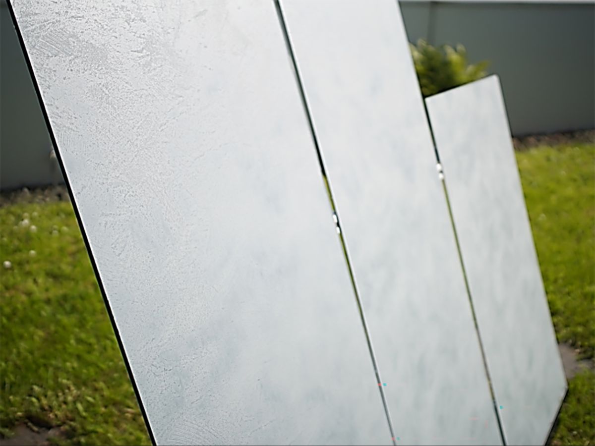 Nahaufnahme der drei Design-PV-Fassadenmodule aus schrägem Blickwinkel. Die Oberflächenstruktur der Dekorfolie in Putzoptik ist deutlich erkennbar. Der Strukturlack erzeugt eine haptisch fühlbare Textur, die konventionellen Baumaterialien nachempfunden ist.	 
