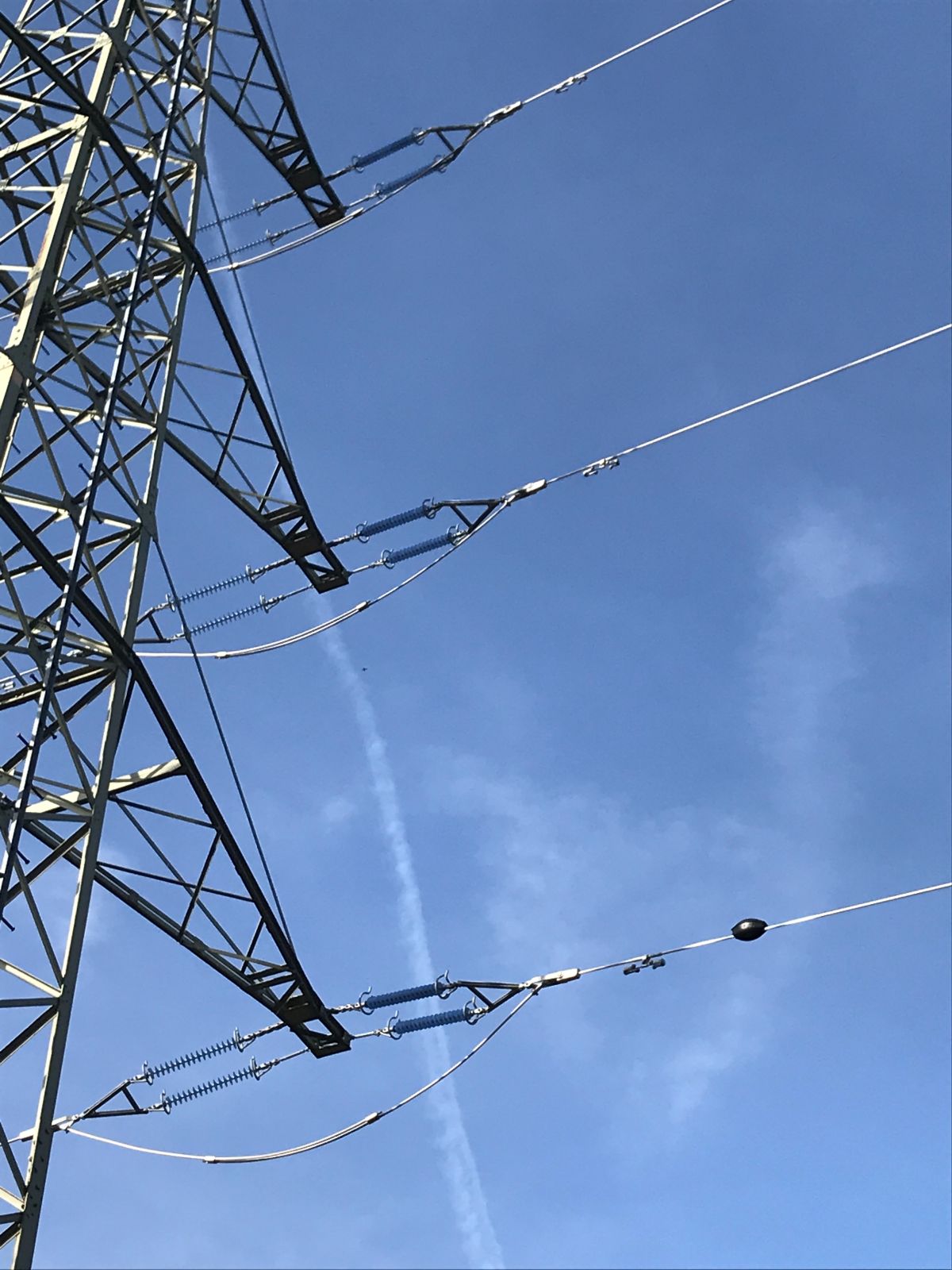 Ausschnitt eines Hochspannungsmasts mit drei Stromleitungen vor blauem Himmel. An der unteren Leitung ist ein schwarzer, ovaler ASTROSE-Sensor befestigt.