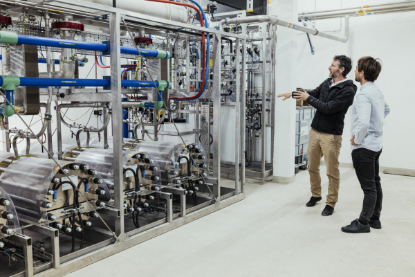 Tobias Nusser vom Steinbeis-Innovationszentrum energieplus steht mit Mann vor der Elektrolyse-Anlage und erklärt deren Funktionsweise.