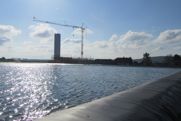 Gefüllter Saisonalspeicher mit Heizzentrale und Pufferspeicher im Hintergrund, 04/25
