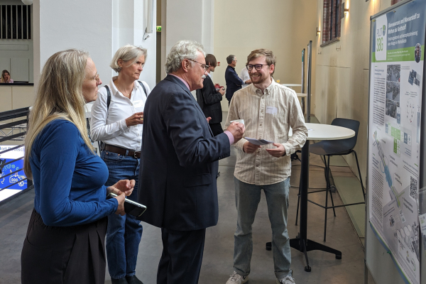 Tagungsteilnehmerinnen und -teilnehmer tauschen sich mit den Nachwuchsforschenden über ihre Projekte während der Poster-Ausstellung aus.