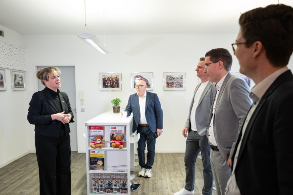 Eine Frau erklärt einer kleinen Gruppe von Personen in einem hellen Raum etwas, während diese aufmerksam zuhören.