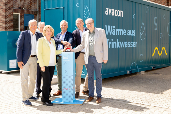 Sechs Personen stehen vor der Pilotanlage zur Wärmegewinnung aus Trinkwasser im Wasserwerk „Rote Bleiche“ in Lüneburg und betätigen gemeinsam einen symbolischen Startknopf.